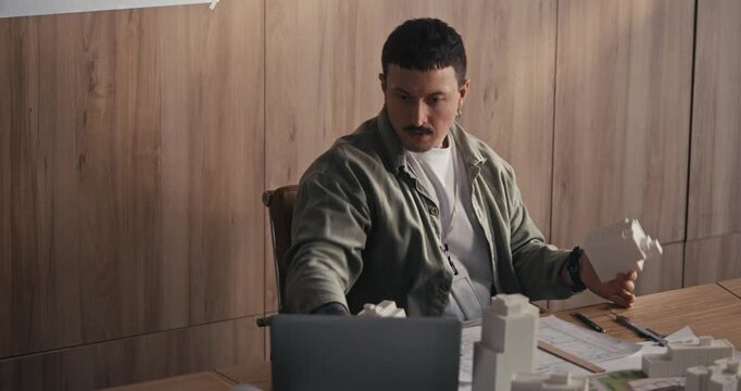 Man works on a model in his office, carefully adjusting pieces and focusing on his design tasks in the morning