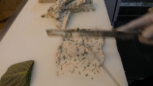 Close-up footage of a professional chef or artisan master skillfully slicing and shaping traditional Korean fish cake, known as eomuk or odeng. The footage shows the thick, savory fish paste mixed wit