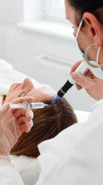 Caucasian girl undergoes scalp treatment to stimulate hair regrowth using microneedling dermapen and vitamin injections. Procedure performed by trichologist in cosmetology clinic for hair restoration.