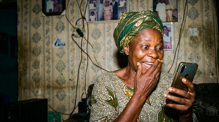 Fototapeta premium Elderly African woman reacts with joy and surprise while looking at her smartphone screen