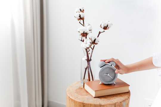 Woman turning off an alarm clock on bedside table in cozy bedroom interior. Morning awakening, sleep quality and daily routine. Concept of biological clock, circadian rhythm. Close up of female hand