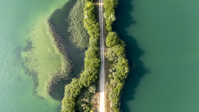 Aerial view of Lagoa da Lontra featuring a narrow dirt path flanked by lush green trees dividing the turquoise and deep green waters in Sandias, Ourense, Spain.