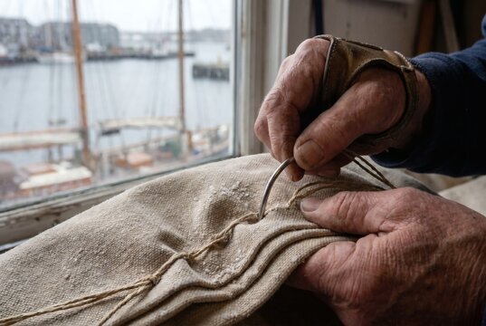 Close Up of Weathered Craftsman Hands Stitching Sailcloth with Needle and Sailmakers Palm Traditional Sail Making Concept