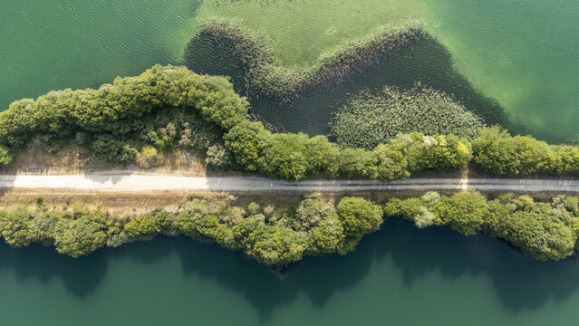 Aerial view of Lagoa da Lontra featuring a narrow dirt path cutting through lush green trees and vegetation between calm turquoise waters Sandias, Ourense, Spain.