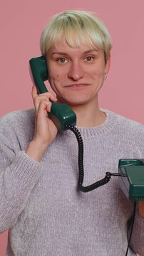 Hey you, call me back. Millennial woman with short hair talking on wired vintage telephone of 80s, says hey you call me back. Young girl isolated on pink background. Lgbt gay lesbian people concept