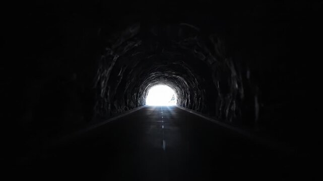 Dark tunnel carved directly into mountain rock face sudden transition from bright daylight to black