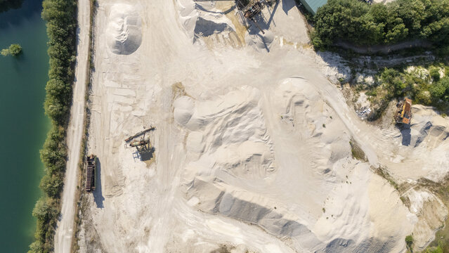 Aerial view of Extraccion de aridos Lima S.L quarry with piles of sand, gravel, heavy machinery, and a water reservoir in Vilarino das Poldras, Ourense, Spain.