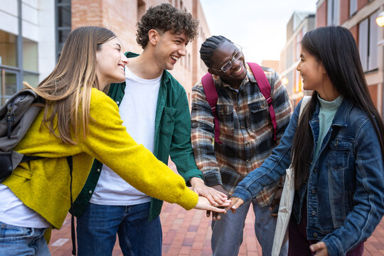 Happy multi-ethnic students joining hands together, smiling and having fun in college campus