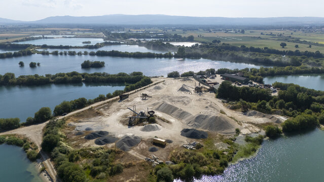 Aerial view of Extraccion de aridos Lima S.L gravel extraction site with piles of sand and gravel, machinery, and surrounding water reservoirs in Vilarino das Poldras, Ourense, Spain.