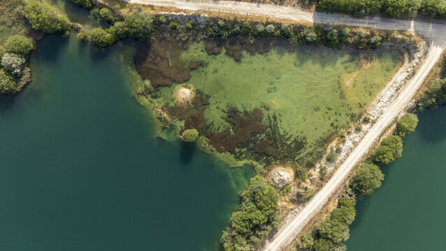 Aerial view of Areeiras da Limia featuring turquoise water pools with green algae patches and a dirt road winding through the landscape in Ourense, Ourense, Spain.