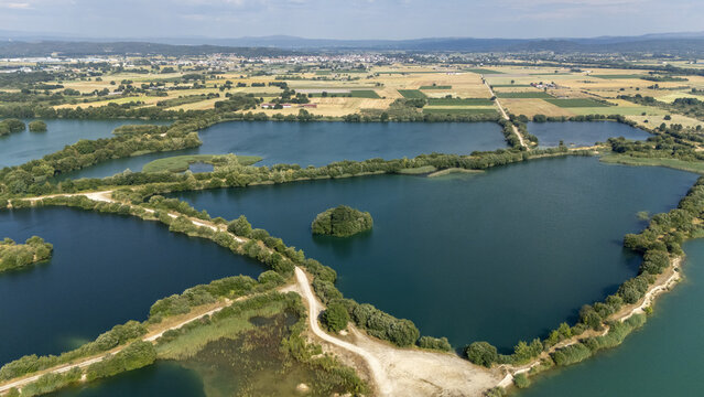 Aerial view of Areeiras da Limia featuring interconnected blue lakes surrounded by lush vegetation, dirt paths, and agricultural fields in Ourense, Ourense, Spain.