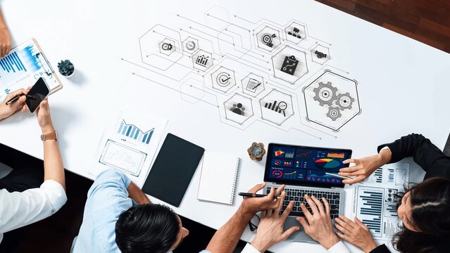A dynamic business meeting featuring professionals analyzing data on laptops and tablets in a modern office, showcasing collaboration and technology. Raster