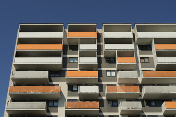Modern apartment building with orange balconies against a clear blue sky, highlighting contemporary residential architecture and geometric patterns © Maciej Bonk