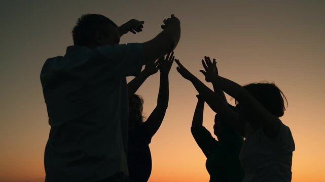 Persons having fun outdoors, dancing on beach, relaxing nature. People dancing to music concert, raising their hands up. Party, dancing, group happy people in evening raising hands to sky. Silhouette