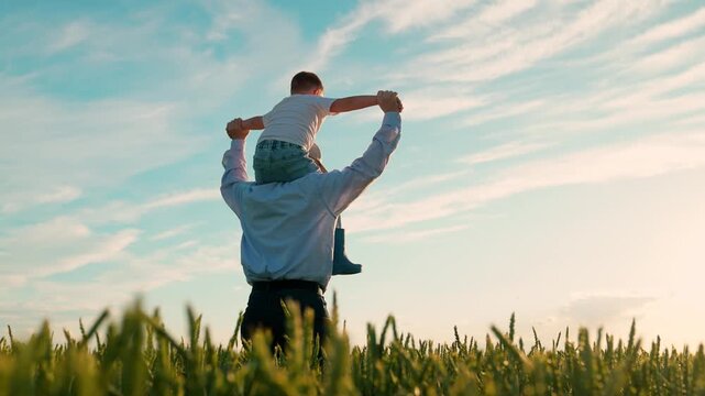 Kid son father play, enjoy nature outdoor, dream of flying, super hero. Family, dad kid with child on their shoulders run through wheat field. Child dreams of fly. Dad, boy child walk together, sky