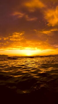 Time lapse video of sunrise over the ocean at Bronte Beach, Sydney, Australia, with glowing red and orange clouds reflected across a gently rippling sea surface.