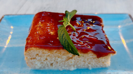 Slice of cake topped with glossy jam and mint leaf on blue plate   © ArtShop