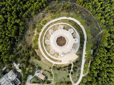 Aerial view of the octagonal Castel del Monte surrounded by dense pine forests and winding paths in Castel del Monte, Abruzzo, Italy.