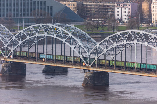 Aerial view of the steel arch railway bridge crossing the Daugava River with a freight train passing over the water in Riga, Latvia.