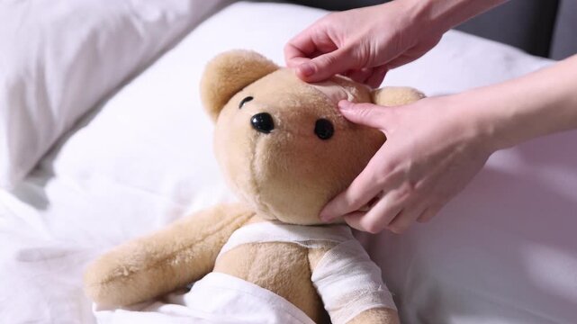 Pediatrician concept. Doctor putting adhesive bandage onto toy bear in bed, closeup