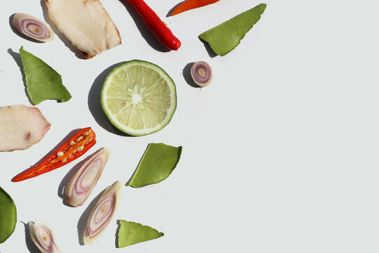 A colorful, close-up pattern of Thai herbs: lime slices, galangal, lemongrass, chilies, and kaffir lime leaves.