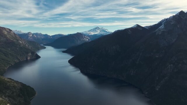 Aerial drone perspective of Brazo Tristeza fjord on Lake Nahuel Huapi with the snow-covered peak of Cerro Tronador in the distance, located in the mountain region of Bariloche, Argentina.