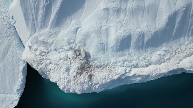 Aerial view of the massive icebergs at Ilulissat Icefjord, showing deep blue water and turquoise light refraction along the jagged white ice edge in Avannaata Kommunia, Greenland.