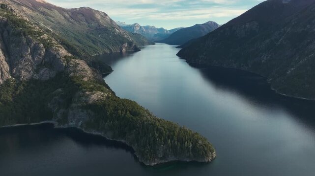 Drone perspective showing a long lake branch surrounded by high mountains and a prominent forested peninsula in Patagonia.