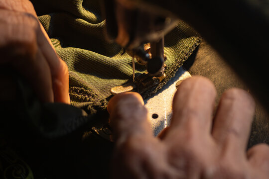 Close up of senior hands carefully guiding a green fabric under the needle of an old vintage sewing machine