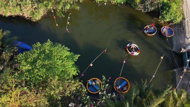 Aerial Hoi An River With Asian Children Splashing From Coracle Boats, Joyful Paddling, Vibrant Round Boats, Buoy Markers, Leafy Banks, Sunlight Sparkle, Carefree Holiday Mood