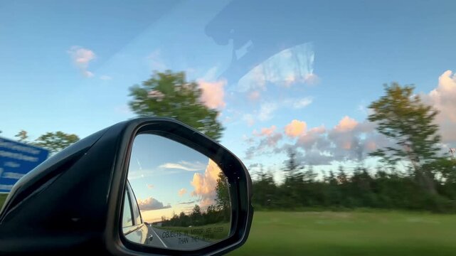Side view mirror reflecting bright sunset sky during road trip