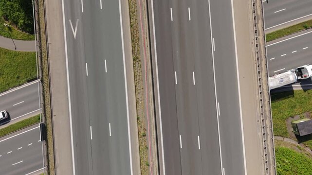 Aerial perspective captures vehicles traveling on a divided highway, including a blue car, red car, and a large truck, illustrating the dynamic movement of traffic in a bright environment