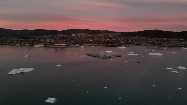 Aerial view of Ilulissat Icefjord with floating icebergs in the calm water under a pink sunset sky in Avannaata Kommunia, Greenland.