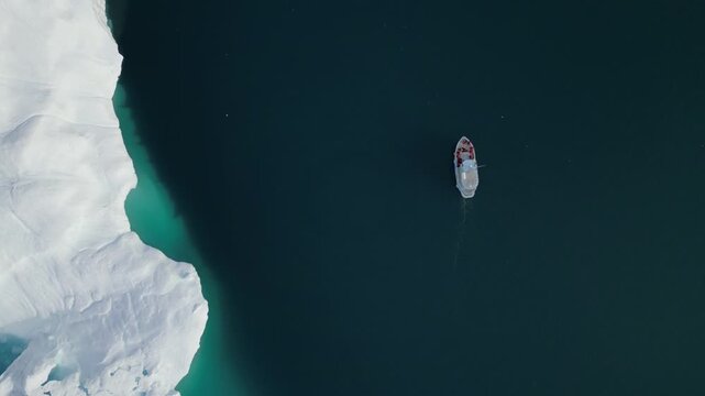 Aerial view of a small boat navigating near a massive iceberg in the dark blue waters of Ilulissat, Avannaata Kommunia, Greenland.