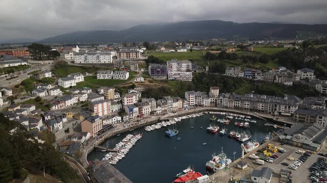 Aerial view of the picturesque harbor filled with fishing boats, surrounded by historic buildings and coastal hills in Luarca, Asturias, Spain.