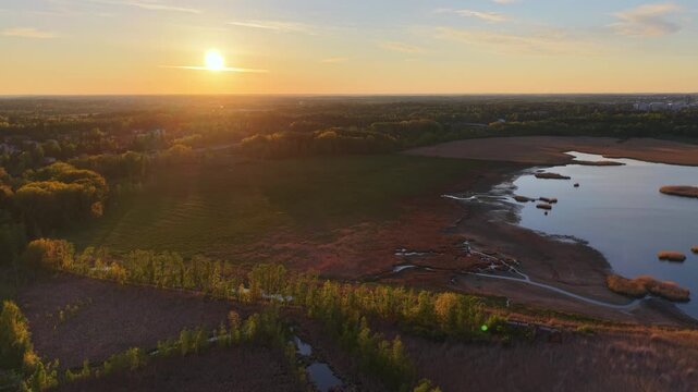 Aerial view of Otaniemi landscape featuring a serene lake, lush trees, and golden sunset light over the fields in Espoo, Uusimaa, Finland.
