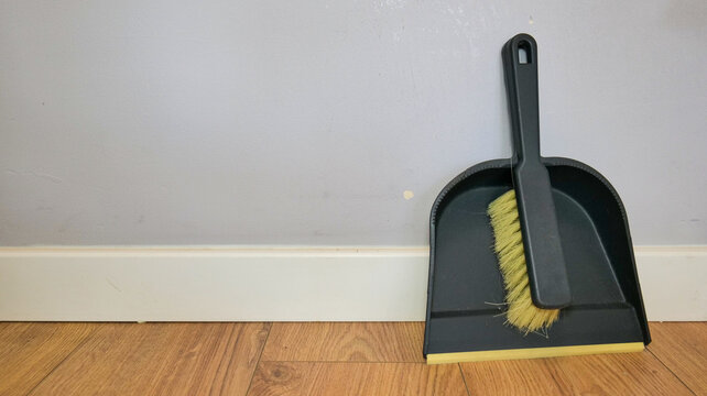 Dustpan and brush standing against a wall indoors. Close-up of household cleaning tools used for everyday home maintenance and cleaning routines