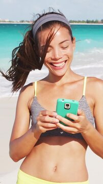 Woman with phone standing on beautiful exotic beach. unrecognizable fitness girl using phone. Video is unretouched and model without makeup. Raw footage. Vertical video.