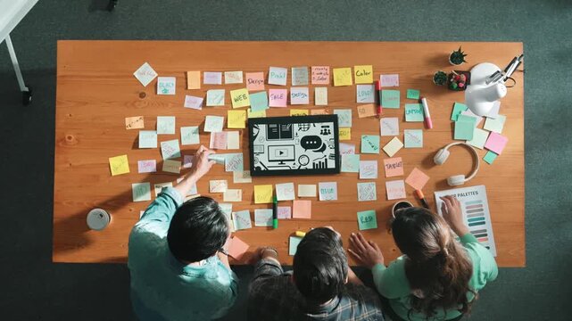 Top view of creative designer working together brainstorming idea by using sticky notes at meeting table with color palettes. Aerial view of smart team choosing icon graphic from tablet. Symposium.
