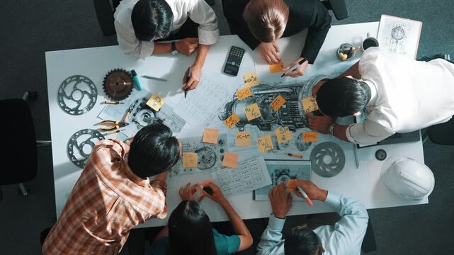 Top view of smart engineer team in casual cloth talking about turbine engine structure at table with metal gear, calculator, sticky notes. Group of technician taking a note in meeting. Alimentation.