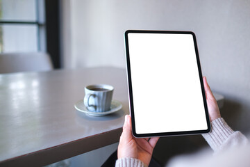 Naklejka premium Mockup image of a woman holding digital tablet with blank white desktop screen in cafe