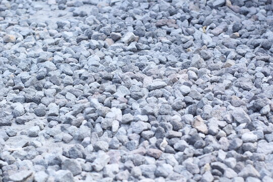 A high-angle, close-up shot of a pile of grey crushed stones and gravel, showing a rough texture suitable for construction, roadwork, or landscaping backgrounds.
