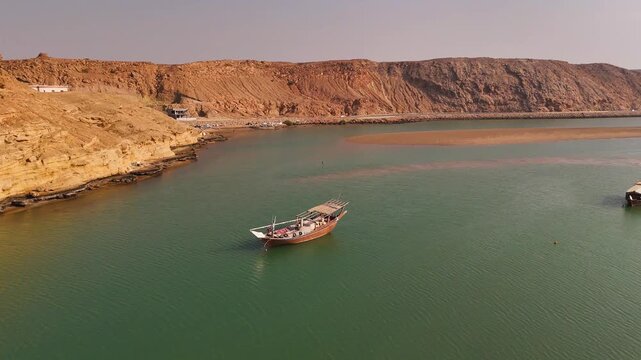 Aerial view of a traditional dhow boat floating in the calm turquoise waters of the bay near the rocky coastline of Sur, Ash Sharqiyah South G, Oman.