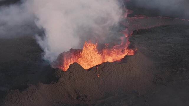 Aerial view of a powerful volcanic eruption with glowing lava fountains and thick smoke plumes rising from the dark basaltic landscape in Grimsey, Reykjanesbaer, Iceland.