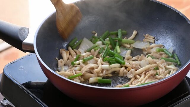 Close up of hand adding spring onion to stir fry oyster mushroom with soy sauce in a hot pan, Asian homemade food