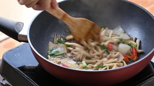 Close up of hand using wooden spatula to stir fry oyster mushroom with soy sauce in a hot pan, Asian homemade food
