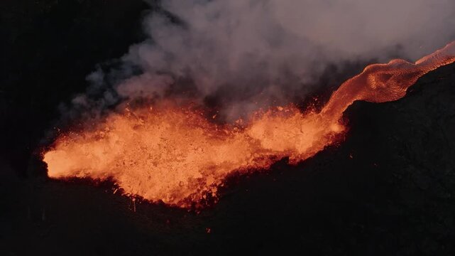 Aerial view of glowing lava flowing from a volcanic eruption with thick smoke rising into the air in Reykjanesbaer, Iceland.