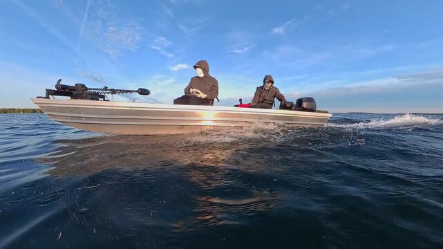 Boat speeding at Lake Couchiching view form side. Two anglers boating in Canadian lake. Side hull view of bass boat with outboard speed motor. Utility boat ride to fishing honey hole spot.