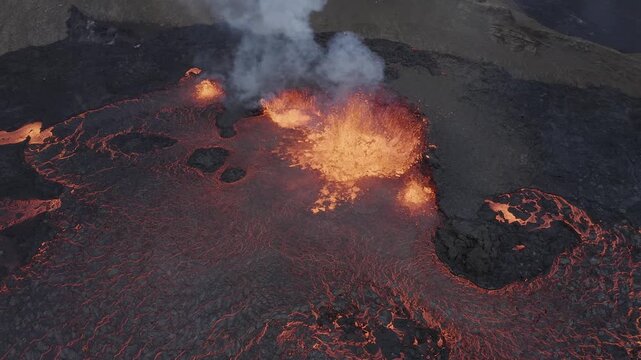 Aerial view of molten lava flowing from a volcanic crater with thick smoke rising into the sky in Reykjanesbaer, Iceland.