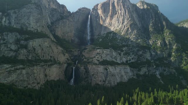 Aerial shot of Yosemite Valley featuring cascading waterfall surrounded by granite cliffs, dense forest, and dramatic mountain landscape in California&rsquo;s Sierra Nevada.